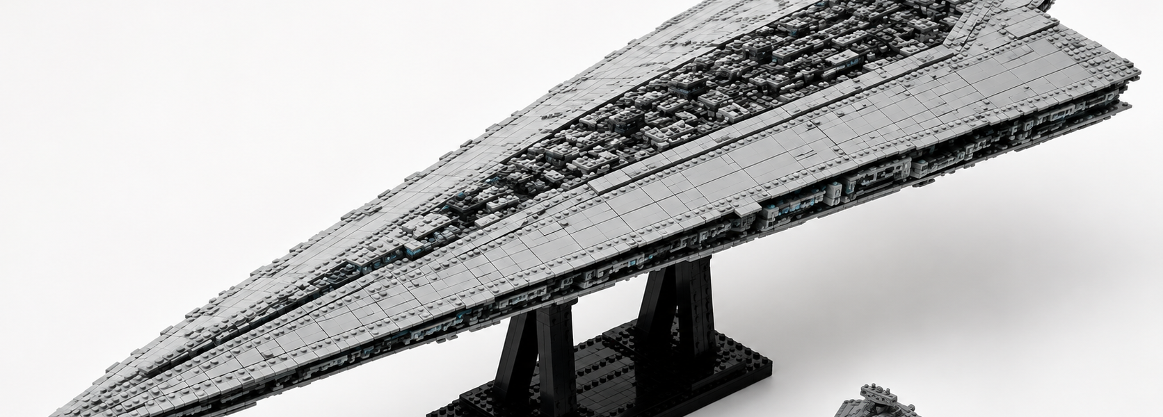 A large gray wedge-shaped brick-built sci-fi starship on a black stand, with a smaller ship beside it to show scale, set against a bright neutral background.
