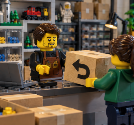 A brick-built seller receives a returned parcel from a customer at a small parts and sets shop counter.