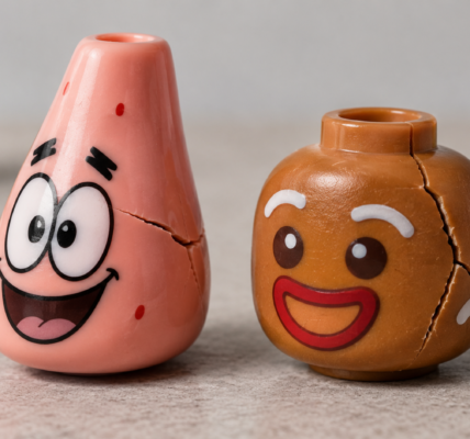 Two stylized toy character heads, one pink and one gingerbread-like, with visible cracks against a neutral studio background.